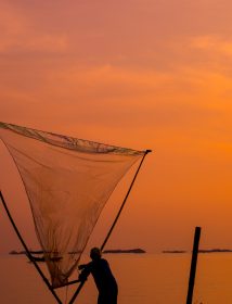 A vertical shot of a beautiful sunset over a sea with a fisherman holding a net